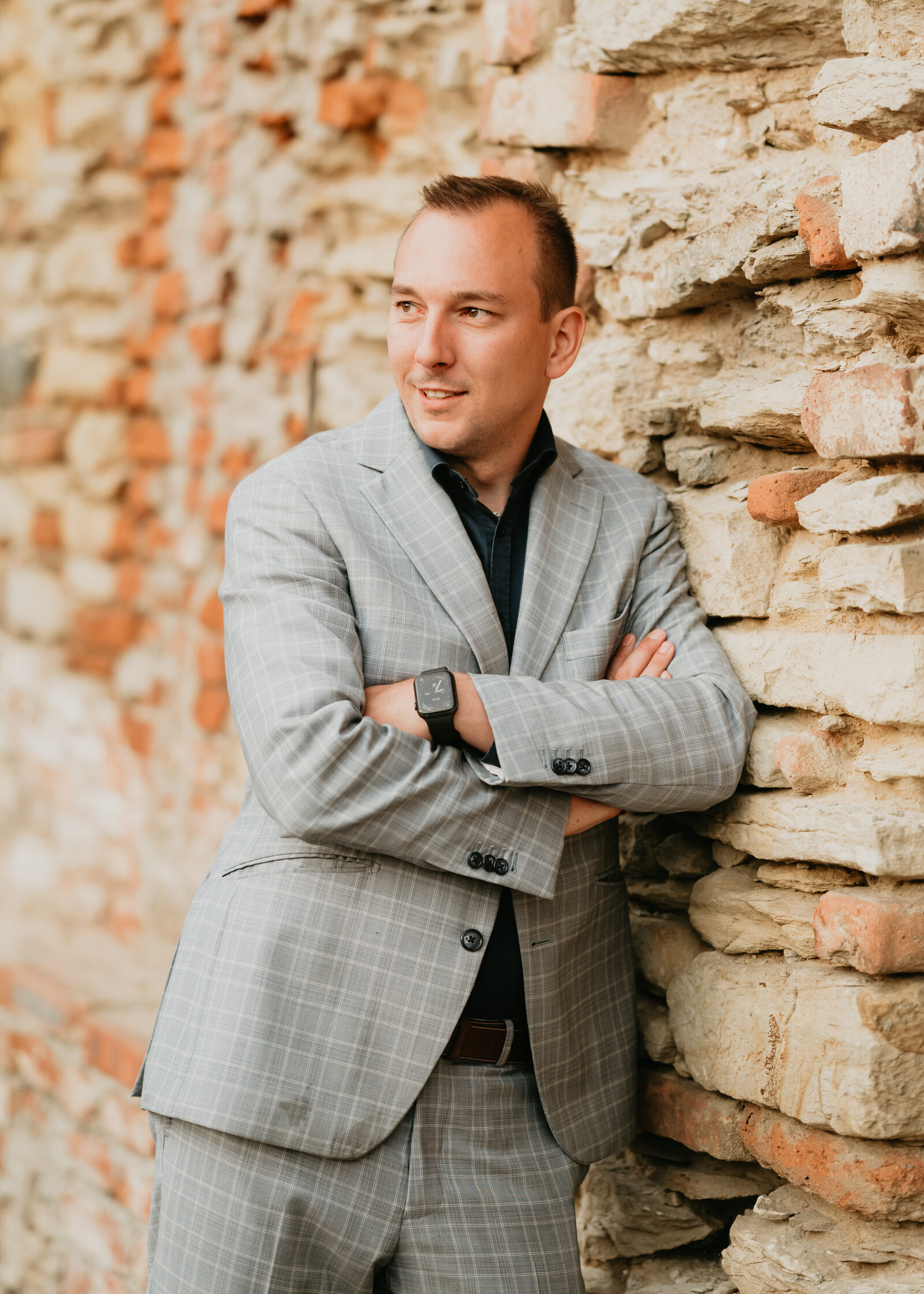 Martin Cihlář v obleku opřený o kamennou zeď svatebního objektu